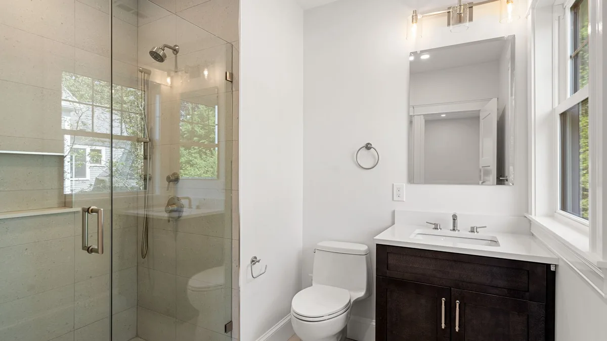 Renovated bathroom with a glass-enclosed shower, tiled walls, dark wood vanity, and chrome fixtures