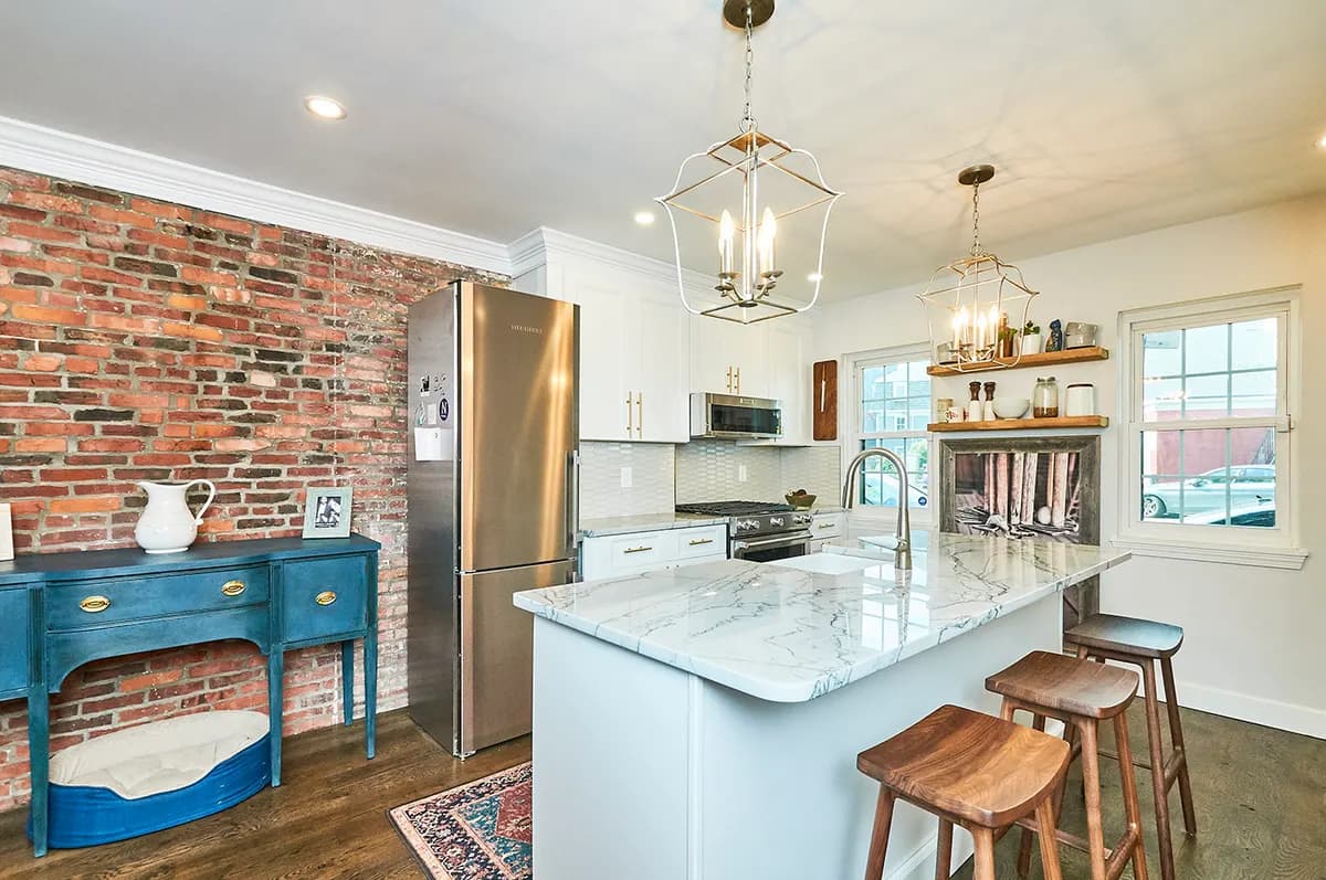 Renovated Cambridge kitchen on 3rd Street with exposed brick, marble waterfall island, and brass pendant lighting