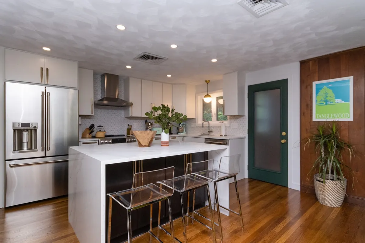 A completed Bay State kitchen remodel on Wallis Rd, Chestnut Hill — light gray shaker cabinets, a marble-look waterfall island, hexagon-tile backsplash, and a stainless refrigerator