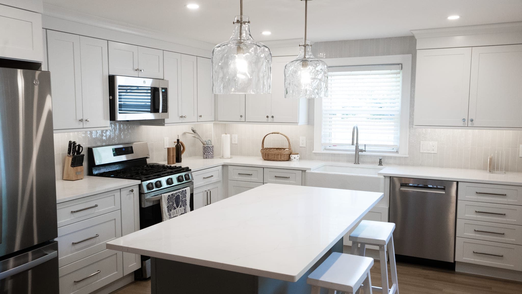 Centre St. West Roxbury kitchen with white shaker cabinets, stainless appliances and an island under two glass pendants
