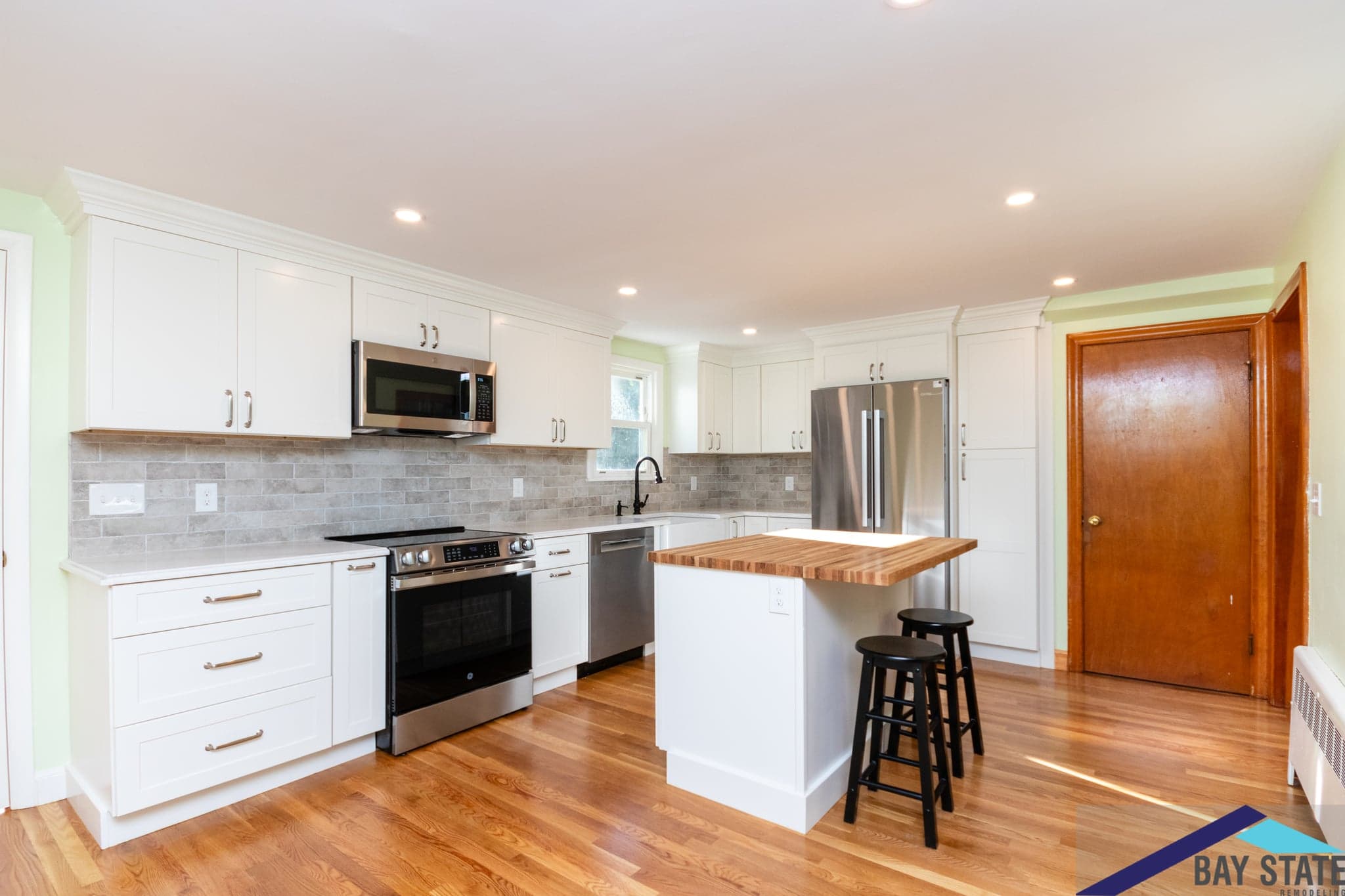 Kingston Rd. Waltham kitchen with white shaker cabinets, gray subway tile backsplash, and butcher block island