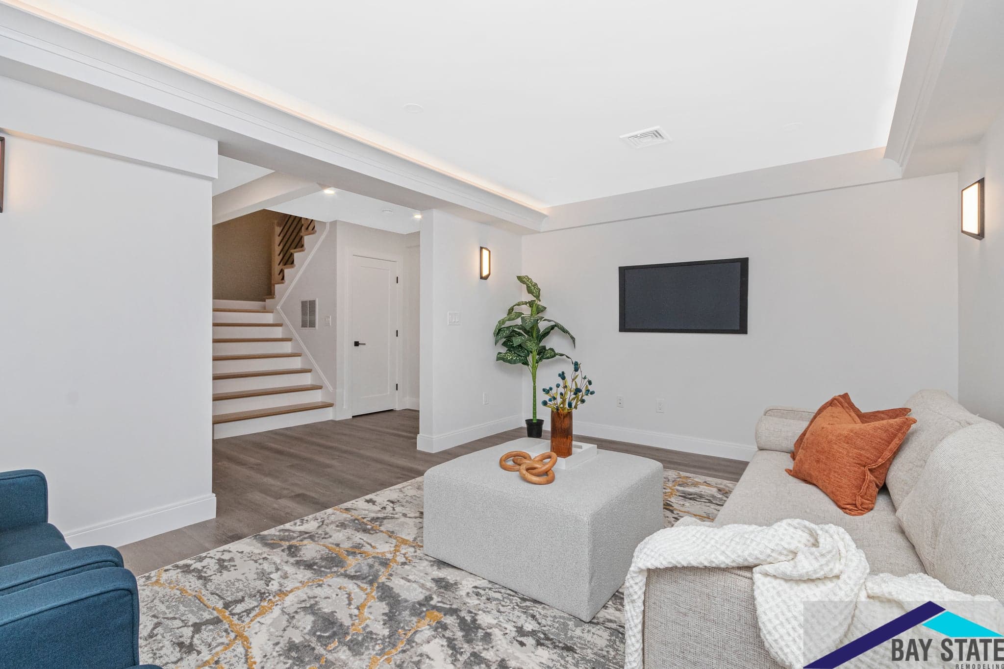 Mill St. Newton basement remodel with a gray sectional, wall-mounted TV, and plank flooring