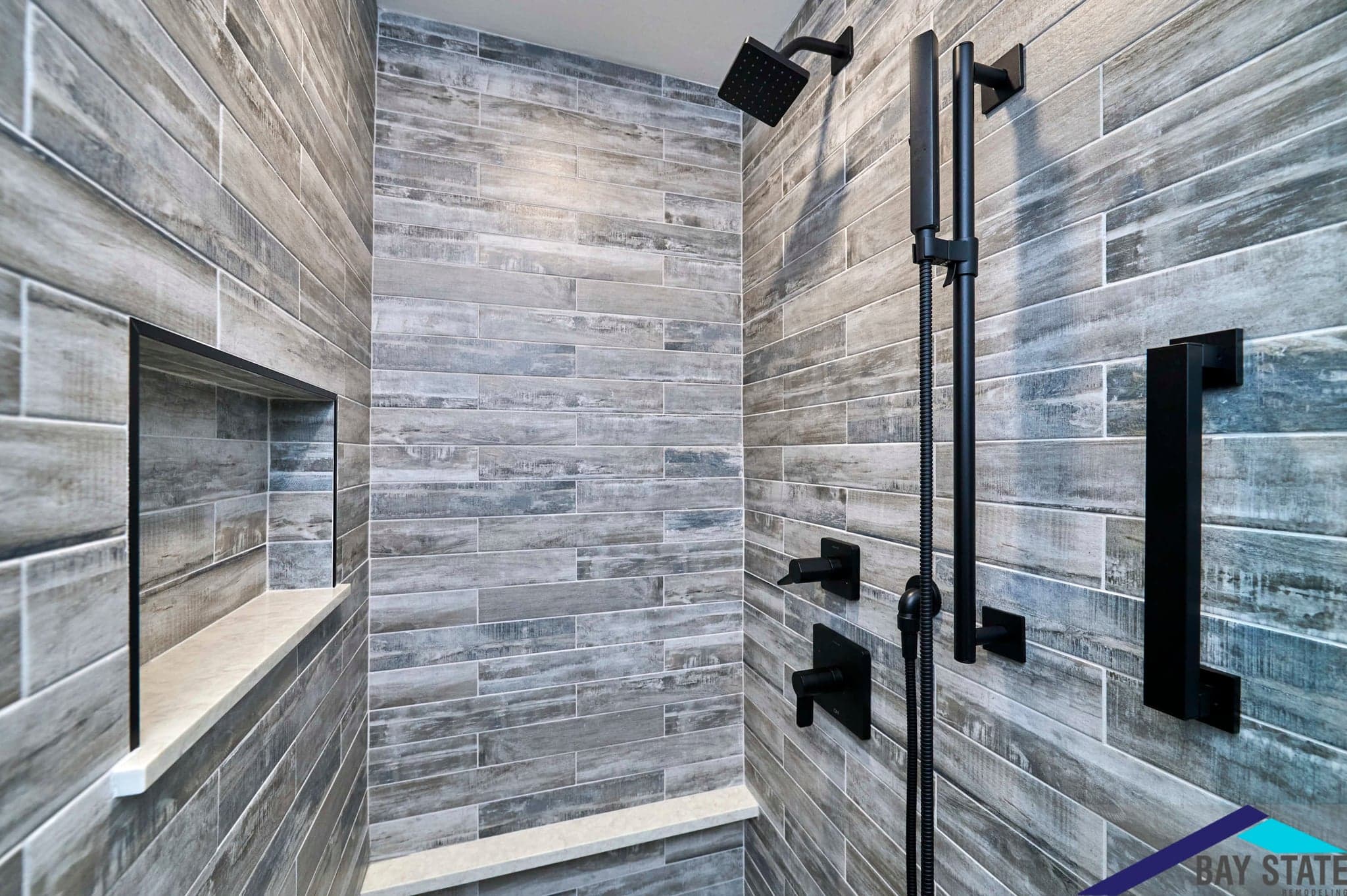 Renovated South Commons Lincoln shower with wood-look gray plank tile, black fixtures, and built-in niche