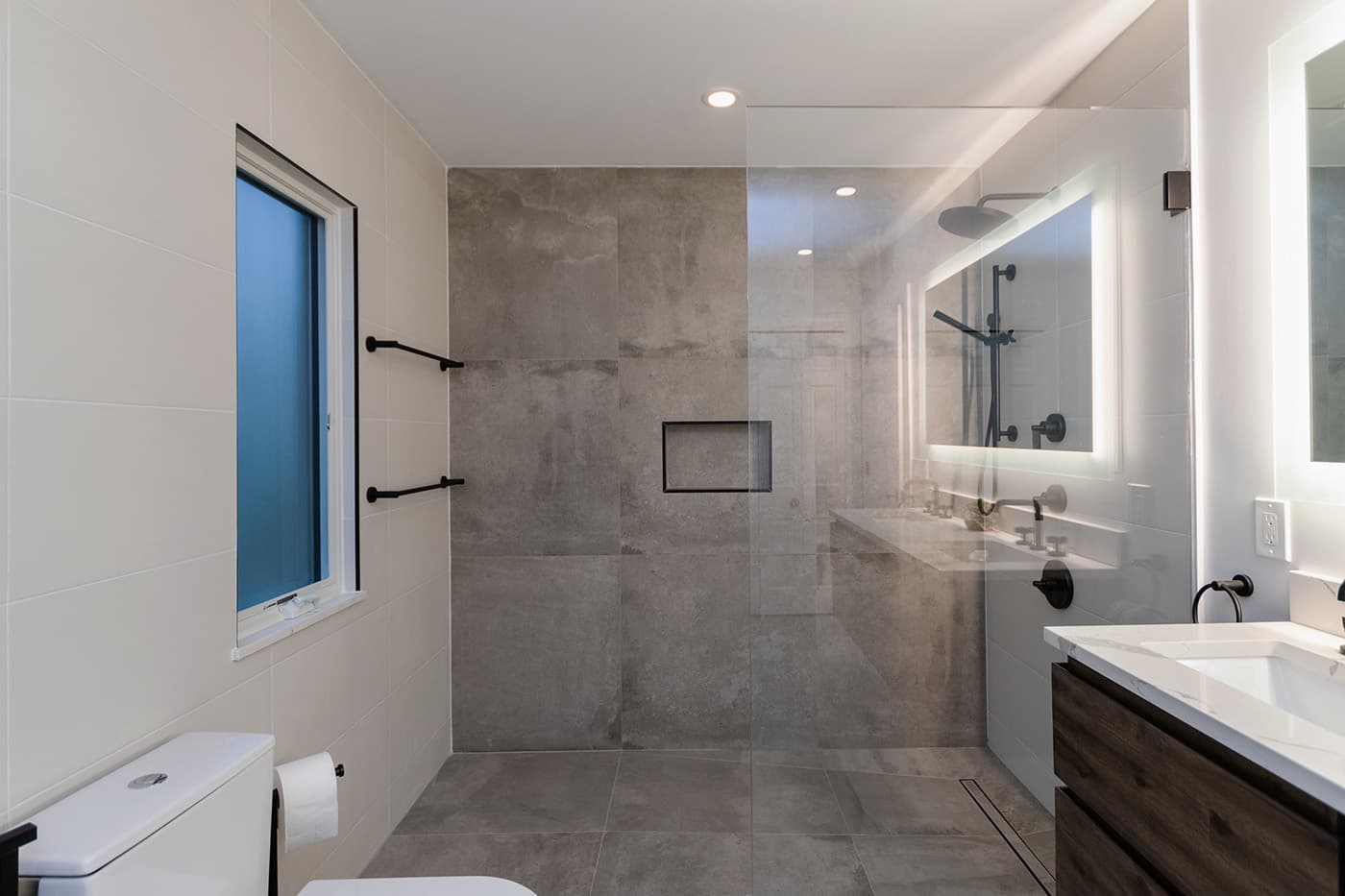 Renovated Amherst Rd. Belmont bathroom with concrete-look tile shower, black fixtures, and a backlit mirror