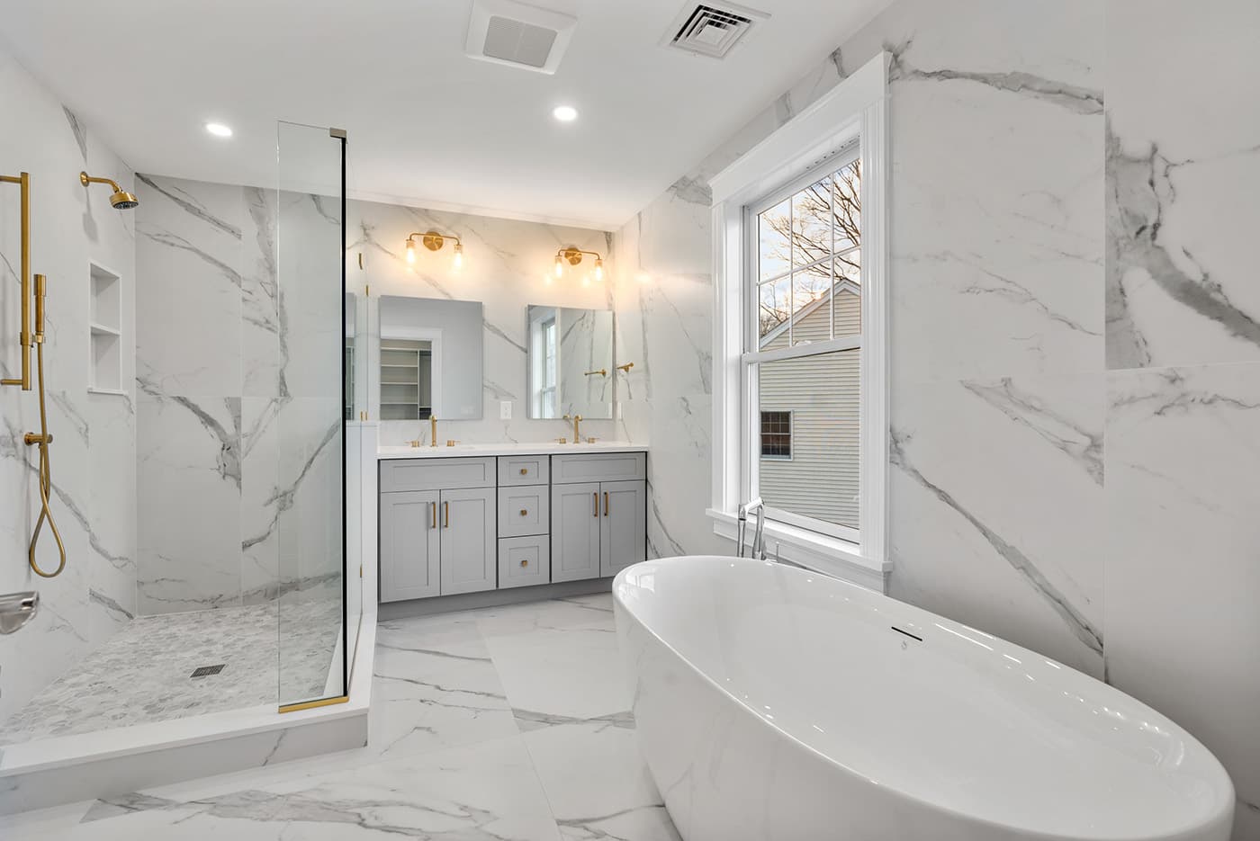 Renovated Auburndale Ave. Newton bathroom with marble tile walls, gold fixtures, and a freestanding tub