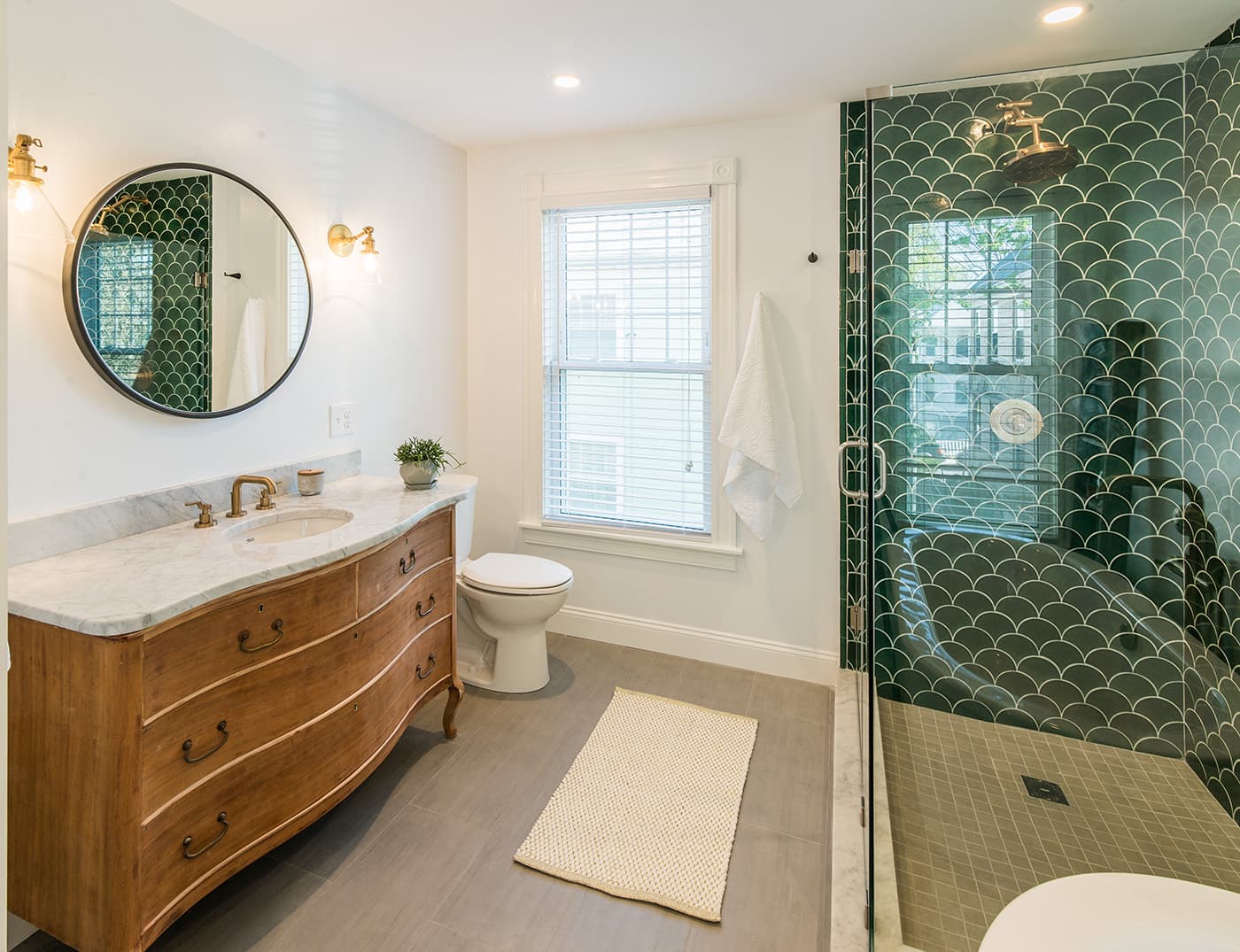 Renovated Bruce St. Dorchester bathroom with antique wood vanity, round mirror, and green scalloped tile shower