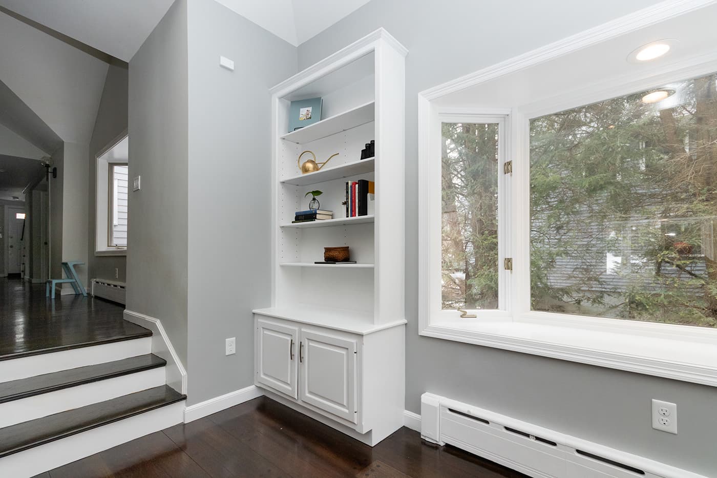 Renovated Columbine Rd. Milton living room shows white built-ins, a bay window seat, and staircase nearby