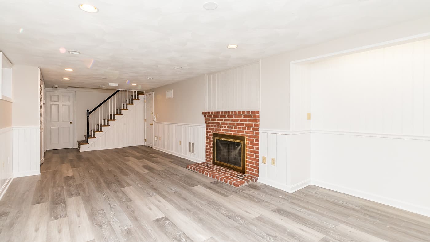 Cross St. Belmont basement finished with a brick fireplace, wainscoted walls, and staircase over wood-look flooring