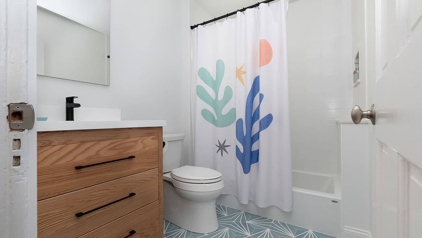 Renovated Dalrymple St. Jamaica Plain bathroom with oak vanity, tub-shower combo, and blue mosaic floor tile