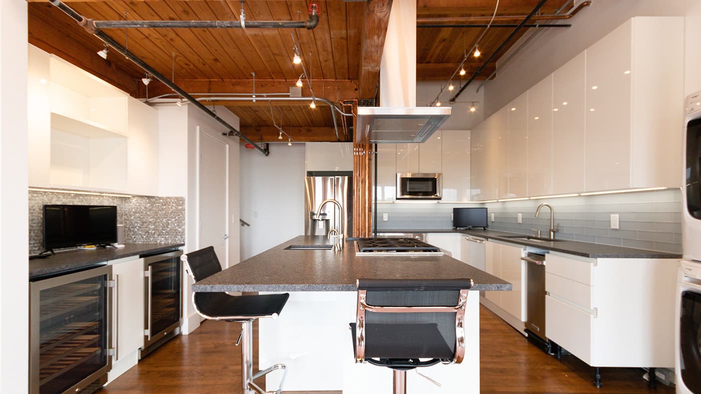 East 1st St. Boston kitchen with glossy white cabinets, speckled granite island, and exposed wood-beam ceiling