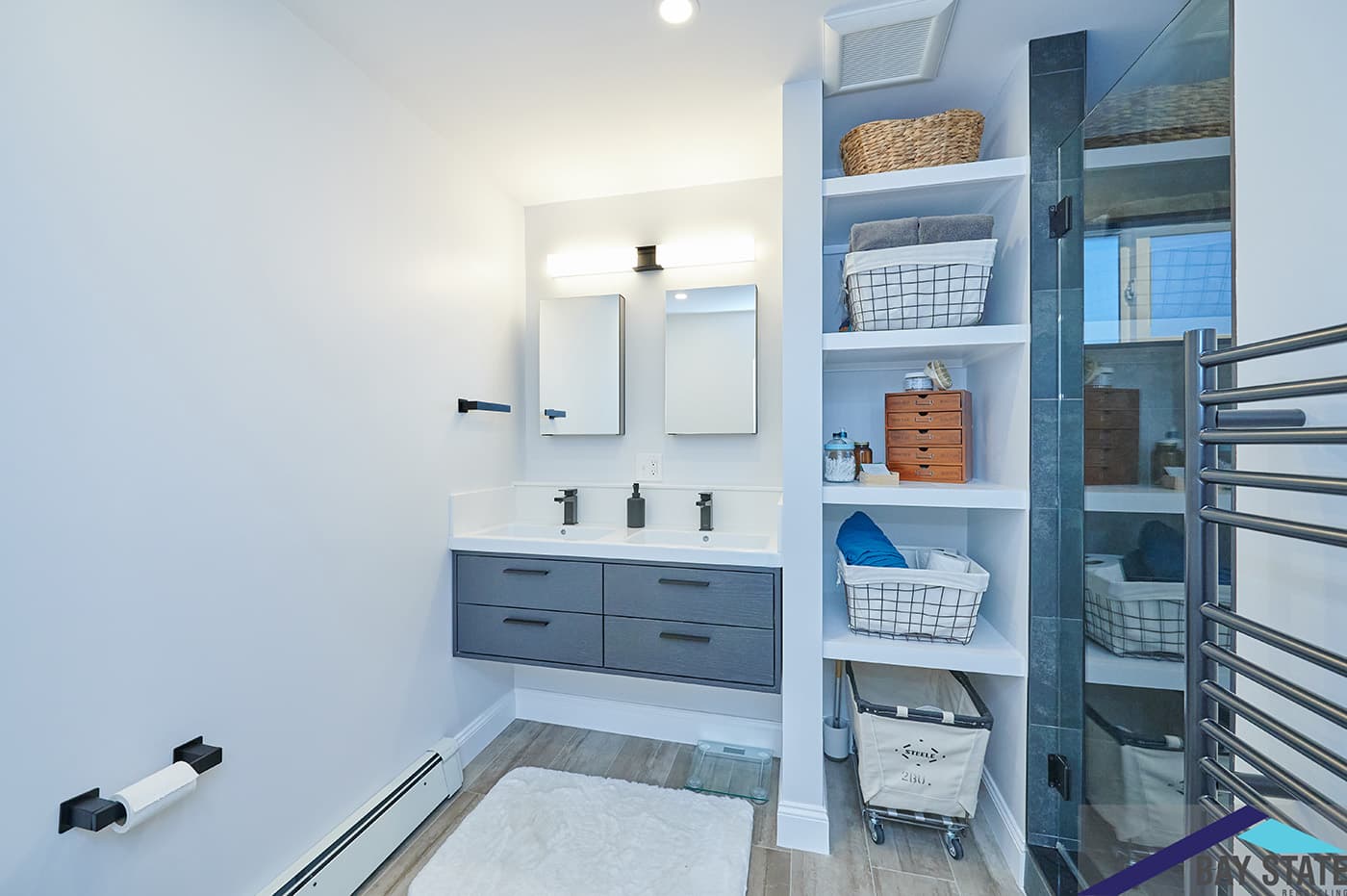 Hinckley St. bathroom after renovation in Somerville, with navy double vanity and tall built-in shelving unit.