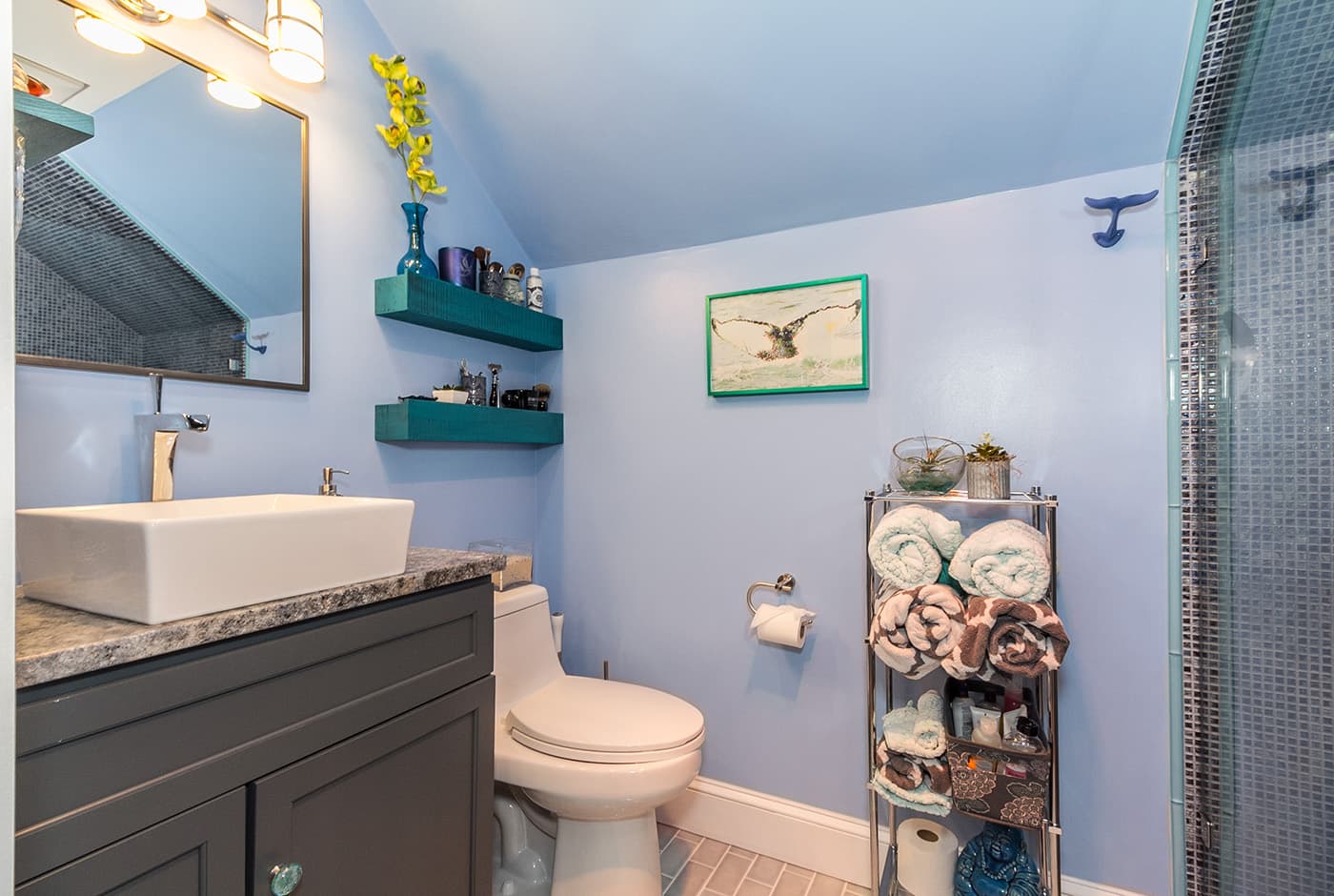 Renovated Minot St. Boston bathroom with lavender walls, teal floating shelves, and vessel sink vanity
