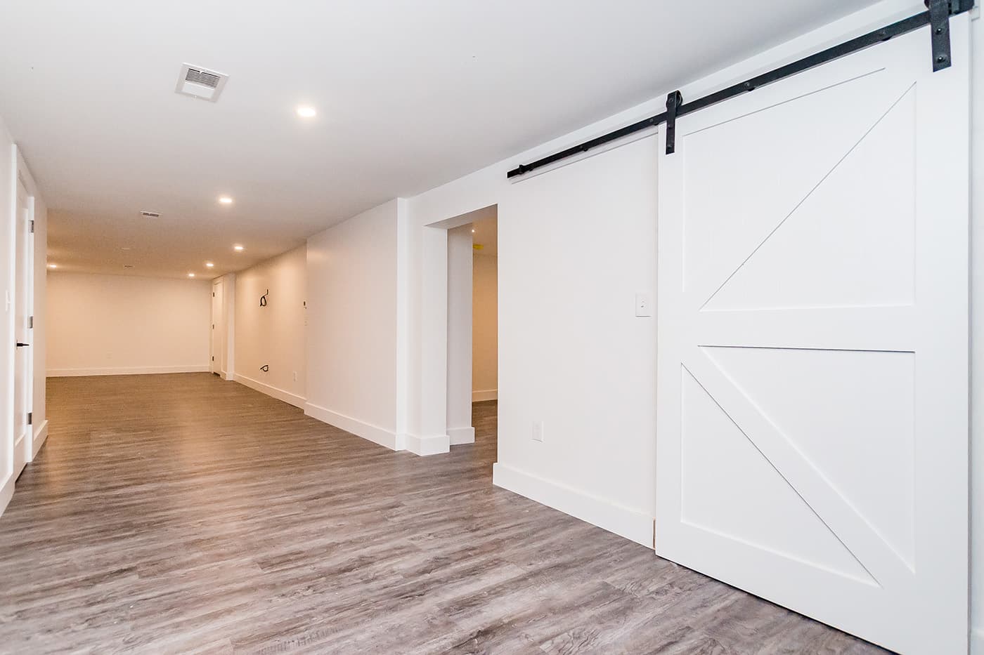 Ridge Ave. Newton basement finished with a sliding barn door, wood-look flooring, and recessed lighting throughout