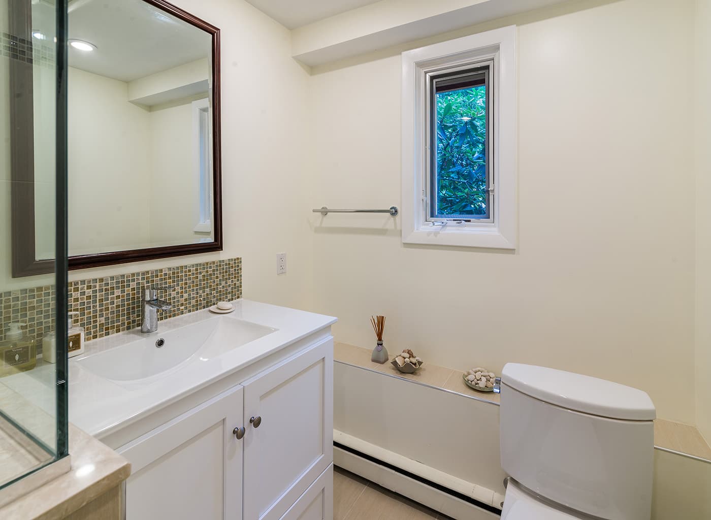 Renovated Rolling Lane Newton bathroom with mosaic tile backsplash, white vanity, and wood-framed mirror
