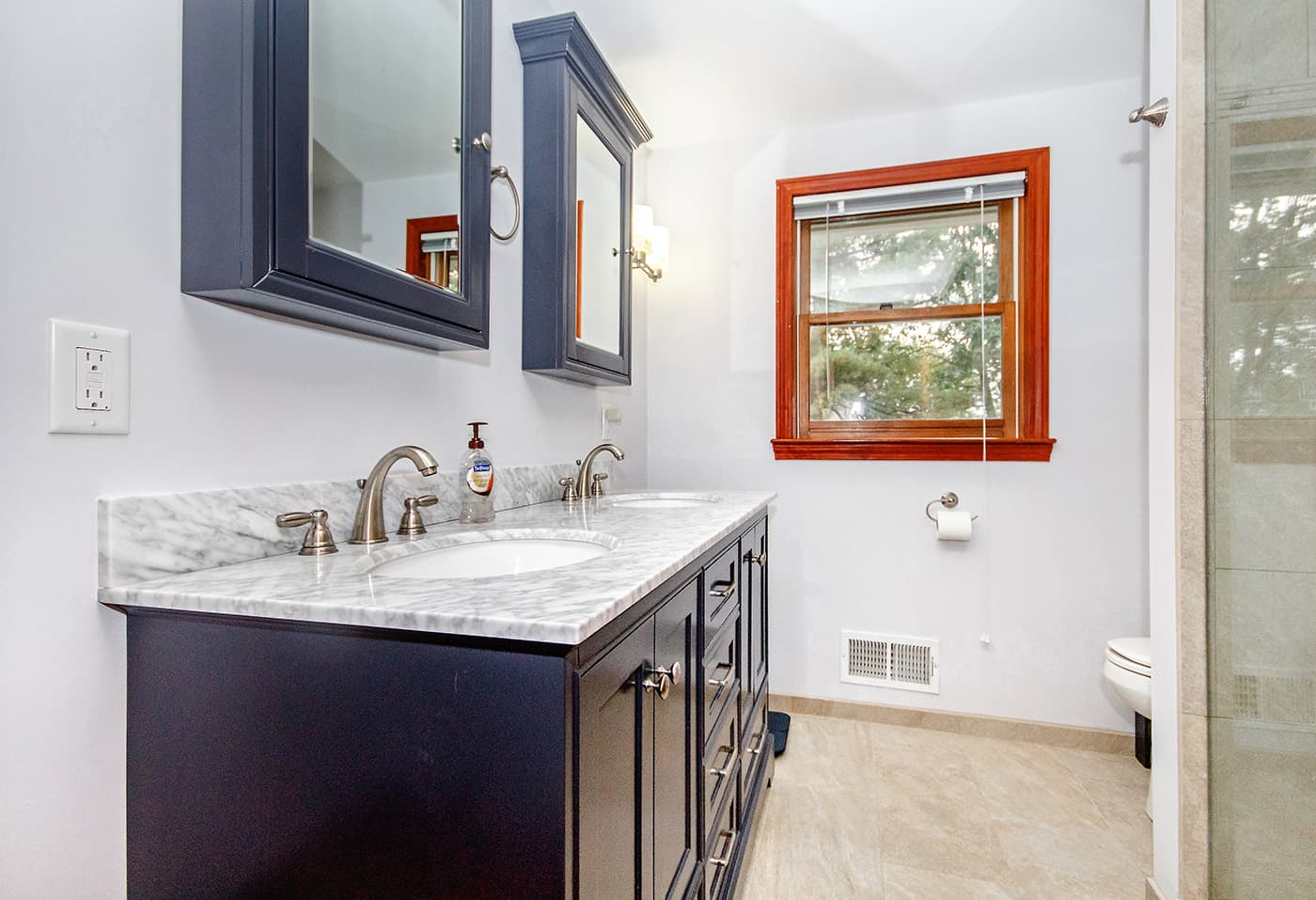 Renovated Rosenna Park Dr. Waltham bathroom with navy medicine cabinets, marble double vanity, and chrome fixtures