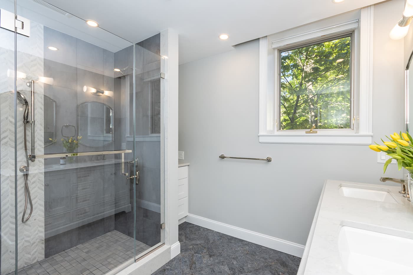 Renovated Sewall Ave. Brookline bathroom with frameless glass shower, wood vanity, and herringbone tile floor