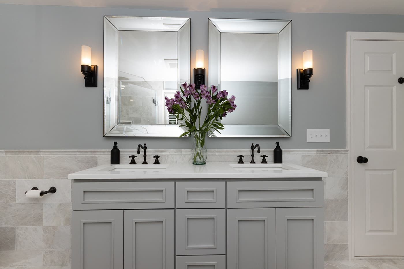 South St. Needham double vanity mirrors with black sconces and purple flowers on the counter