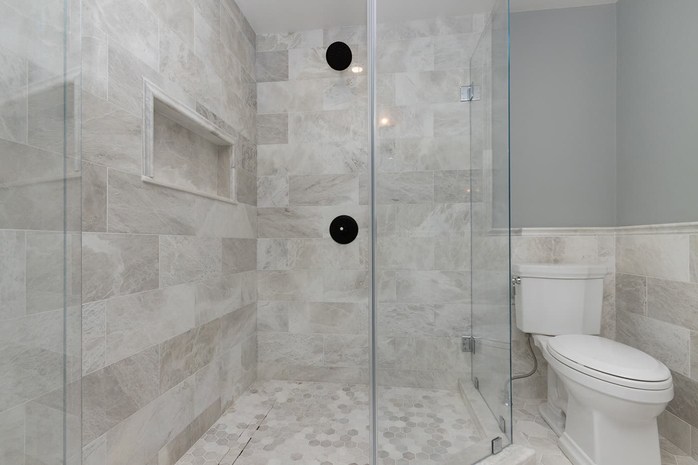 South St. Needham glass shower interior with stone tile, a niche shelf, and two shower controls