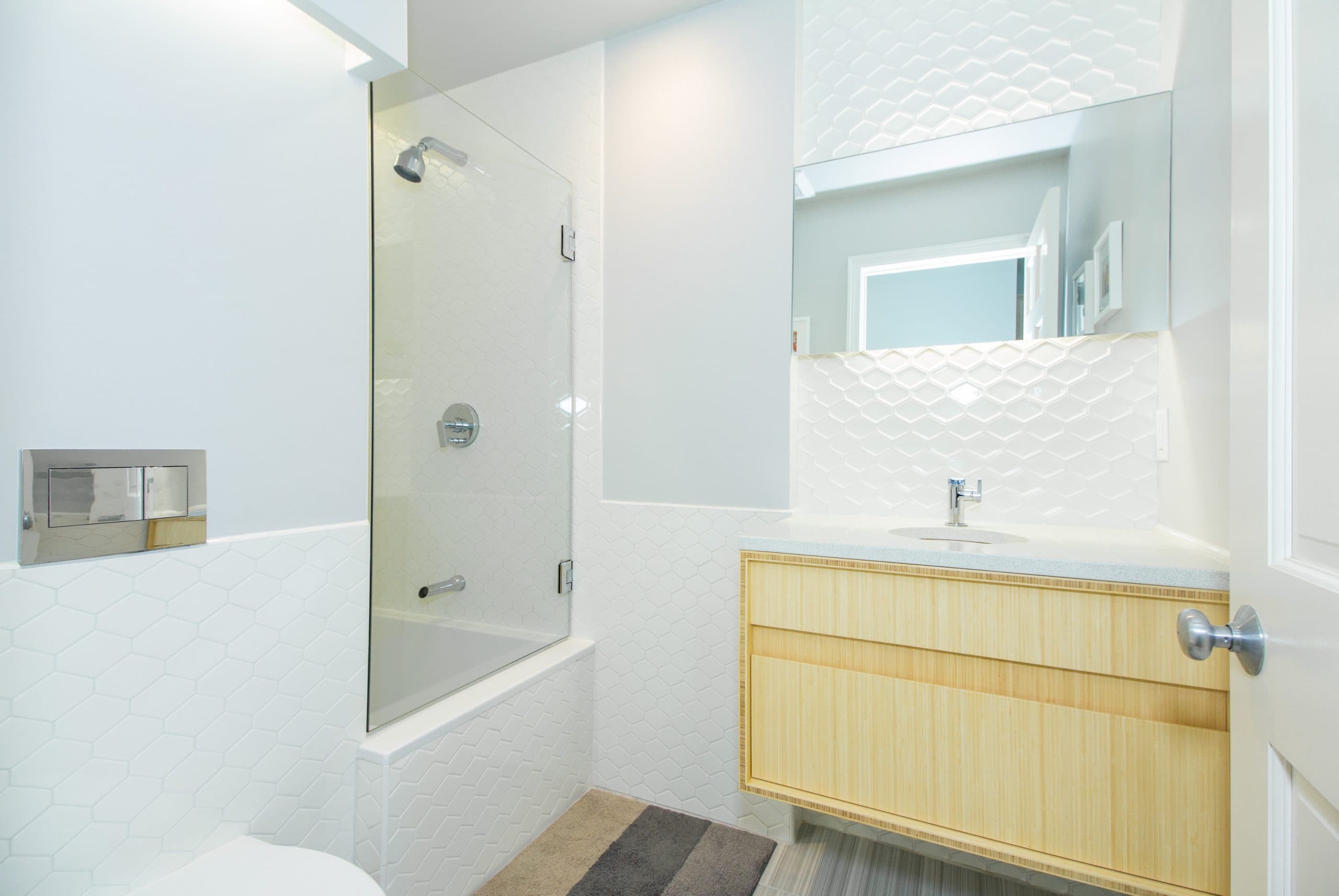 Renovated West Broadway Boston bathroom with white hexagon tile, wood vanity, and a glass shower door