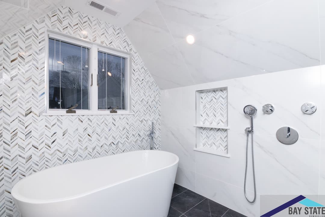Renovated Hunnewell Ave. Newton bathroom with gray tile tub surround, wall-mount toilet, and white vanity