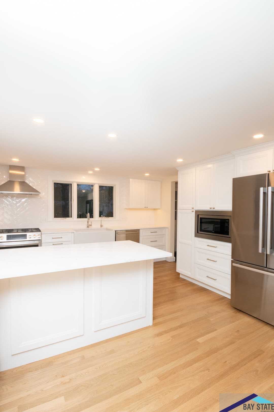 Sun Hill Ln. Newton kitchen after renovation, with white cabinetry, built-in stainless fridge, and quartz island