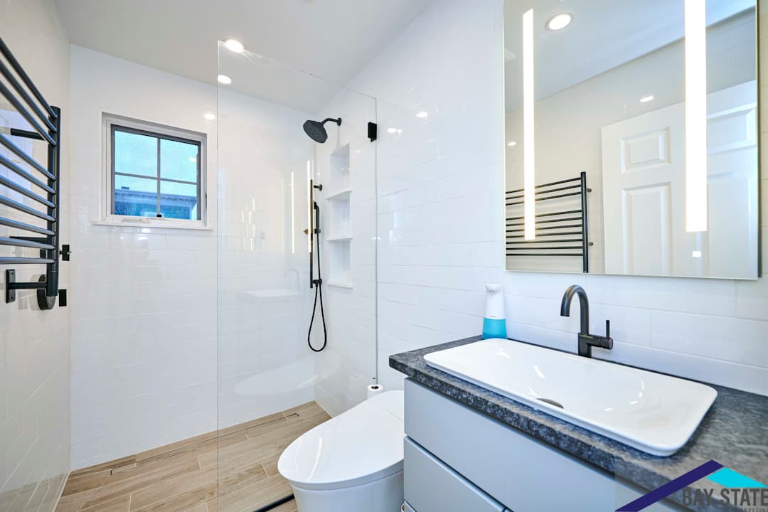 Renovated Harvey St. Cambridge bathroom with white vanity, marble tile shower, and a backlit mirror cabinet