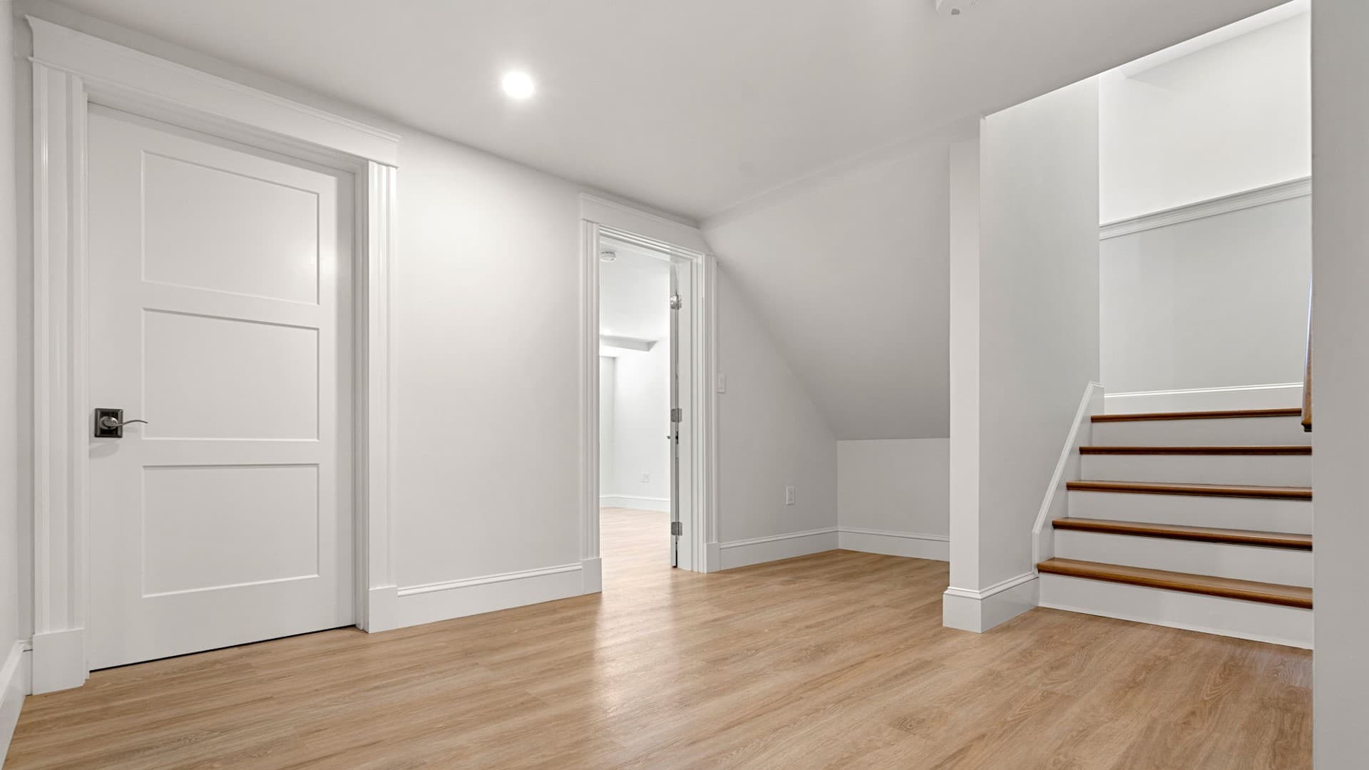 Sewall St. Newton basement finished with light wood flooring, white trim, and open staircase landing