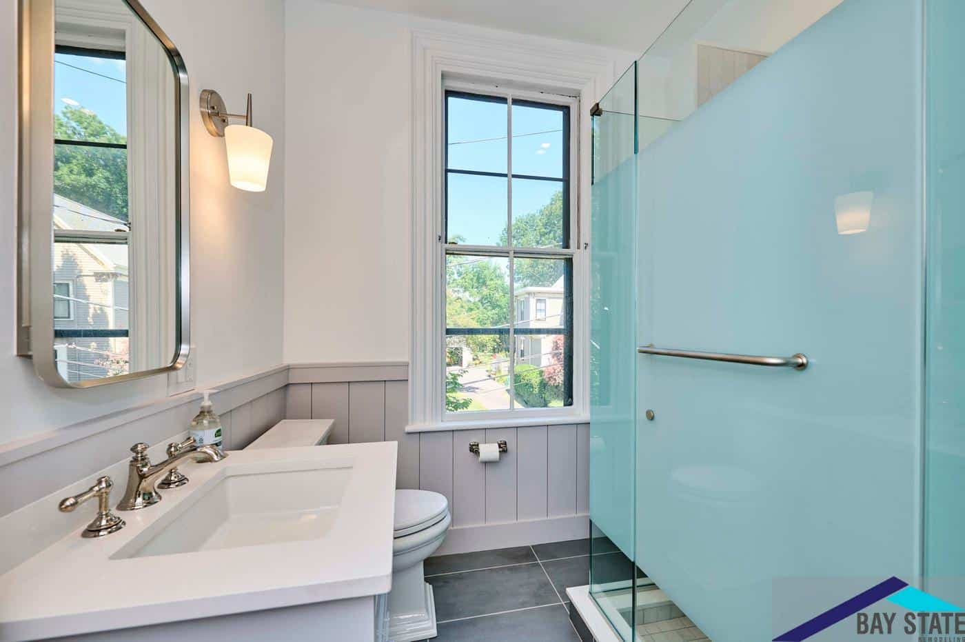 Tennyson St. Somerville bathroom with gray wainscoting, white quartz vanity, and blue glass shower door