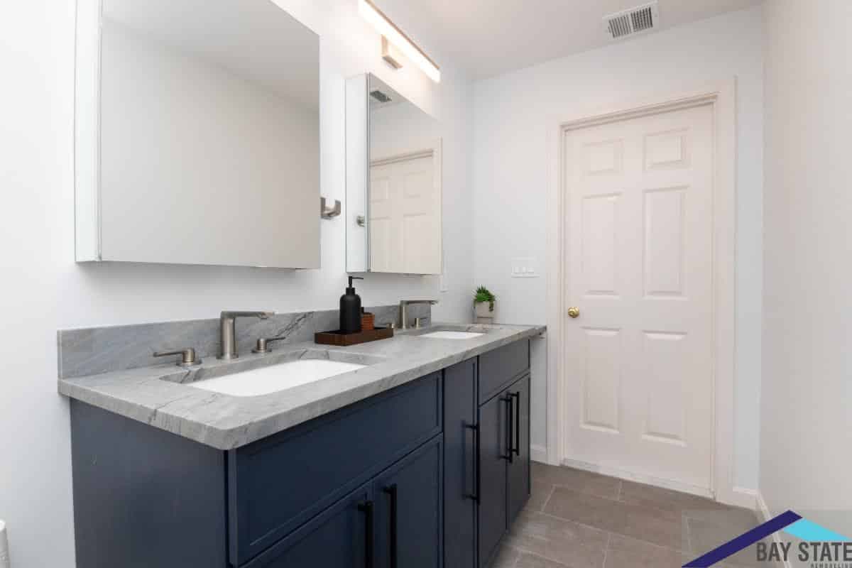 Renovated Conant Rd. Weston bathroom with navy double vanity, gray marble counter, and matching mirrors