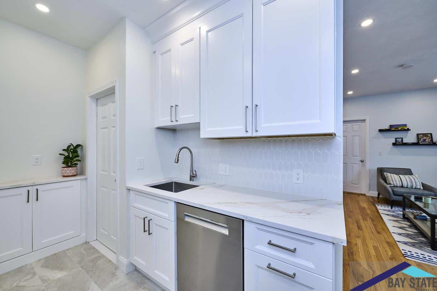 Renovated Norfolk St. Cambridge kitchen opens to living room with hardwood floors and white cabinetry