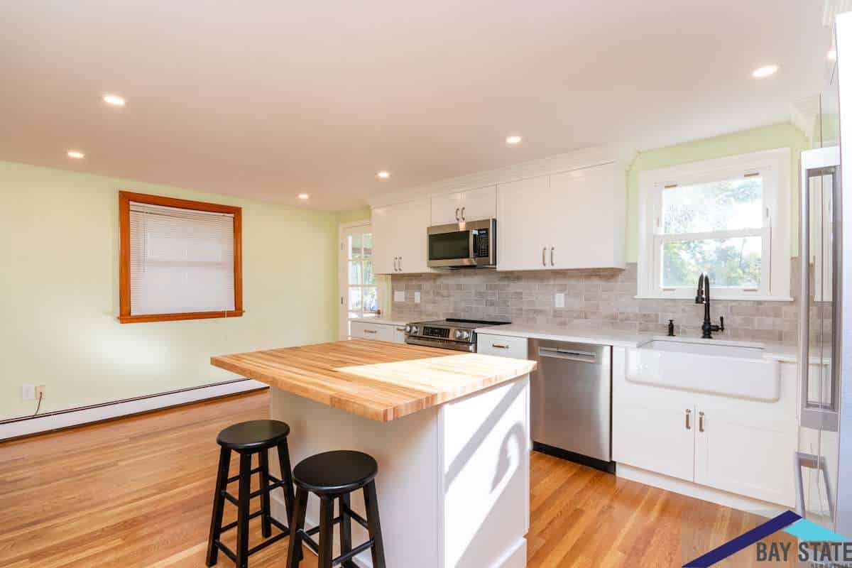 Kingston Rd. Waltham kitchen with white cabinetry, black faucet, and butcher block island seating