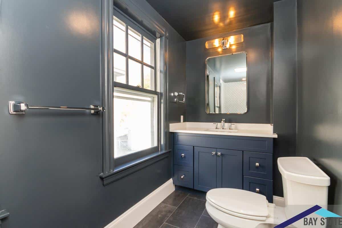 Renovated Bartlett Crescent Brookline powder room with navy walls, chrome fixtures, and an arched mirror