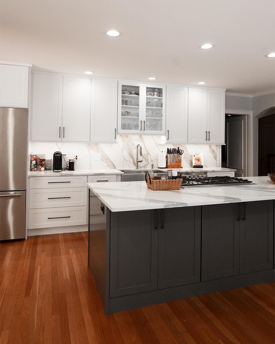 Renovated Wayland kitchen on Brook Trail Rd. with white cabinetry, charcoal island, marble backsplash, and hardwood flooring
