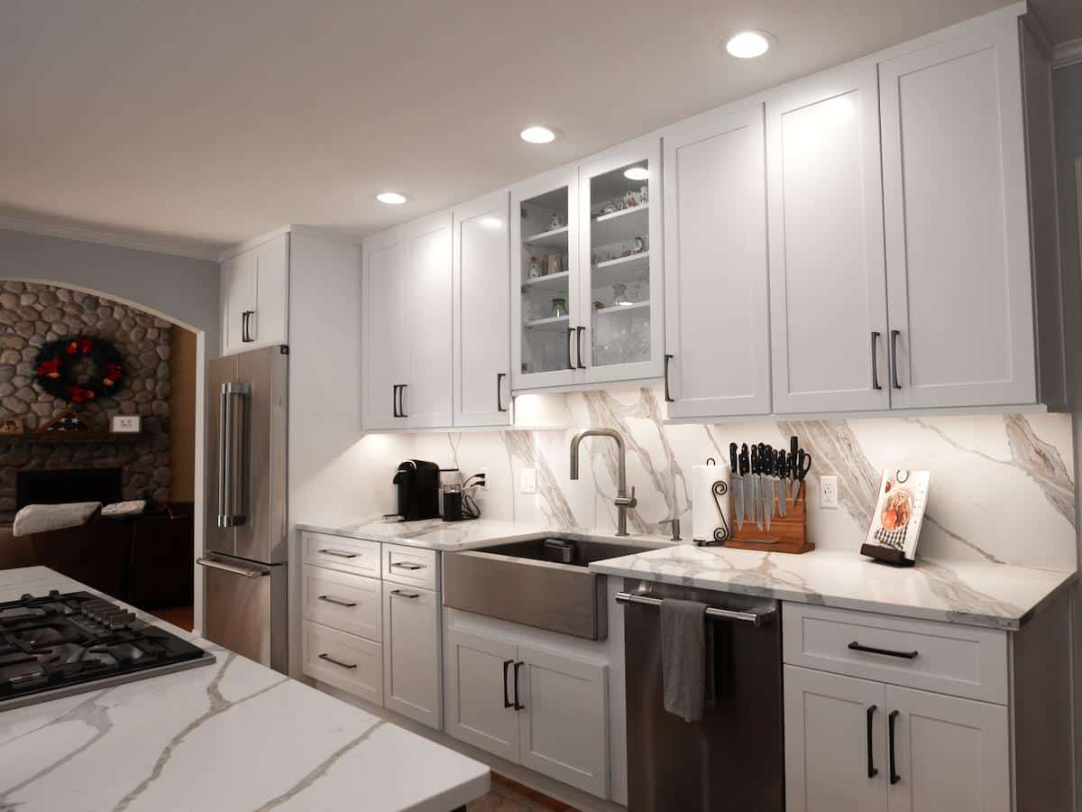 Renovated Wayland kitchen sink wall on Brook Trail Rd. with farmhouse sink, marble backsplash, and stone fireplace nearby