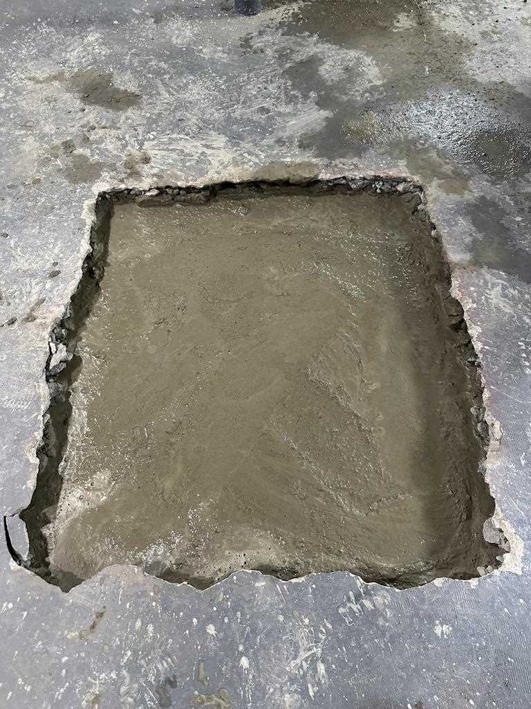 Concrete section of floor cut out and filled with freshly poured concrete, showing initial phase of kitchen remodeling.