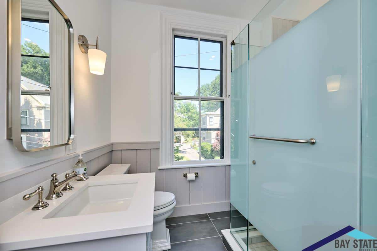 A remodeled bathroom featuring a modern sink with a large mirror, a sleek shower with glass doors, and a window providing natural light.