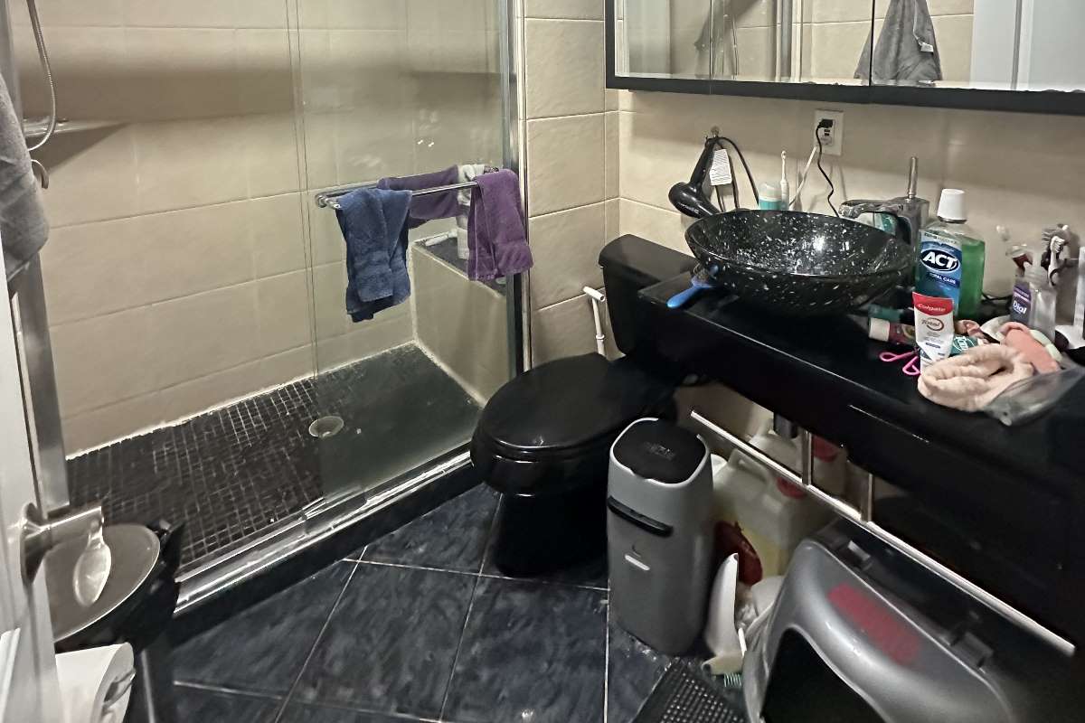 Outdated bathroom with cluttered vanity, dark tones, and old shower before remodeling in Newton, Kensington Ave project.