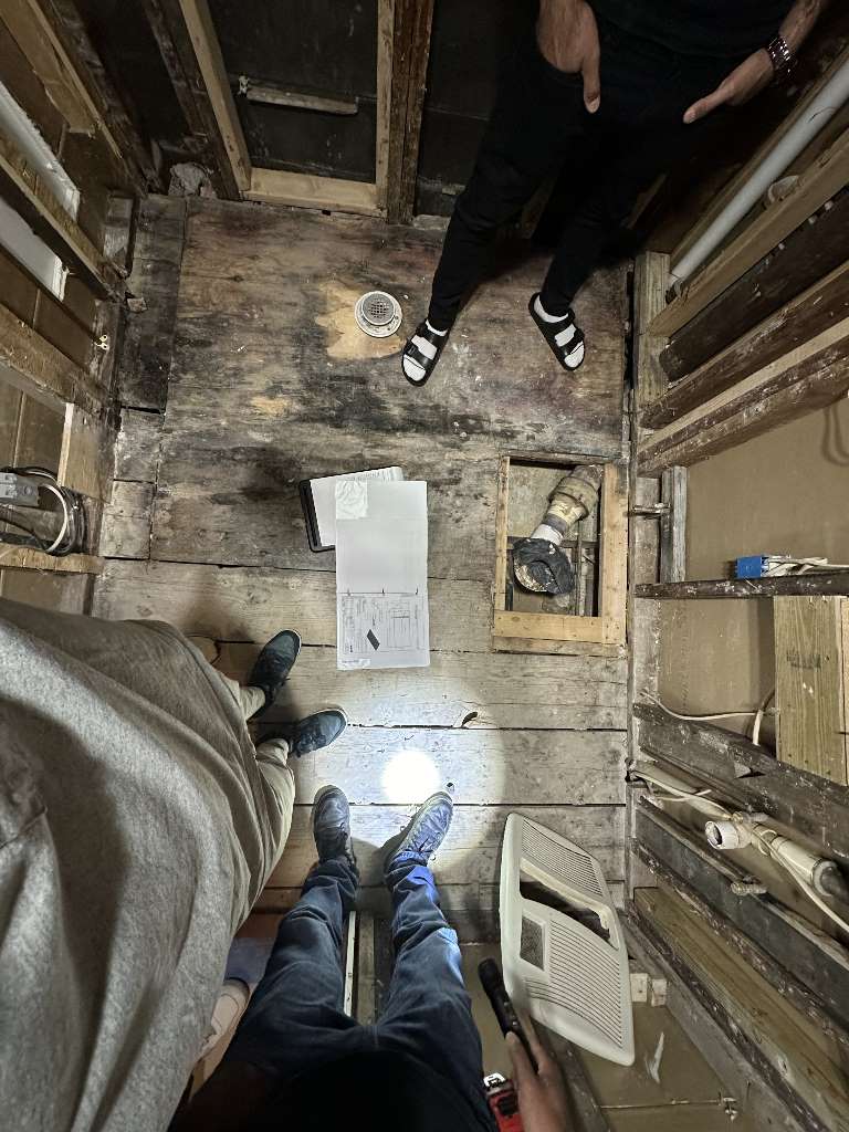 Bathroom renovation in progress with exposed subfloor and workers inspecting plans, Kensington Ave, Newton project.