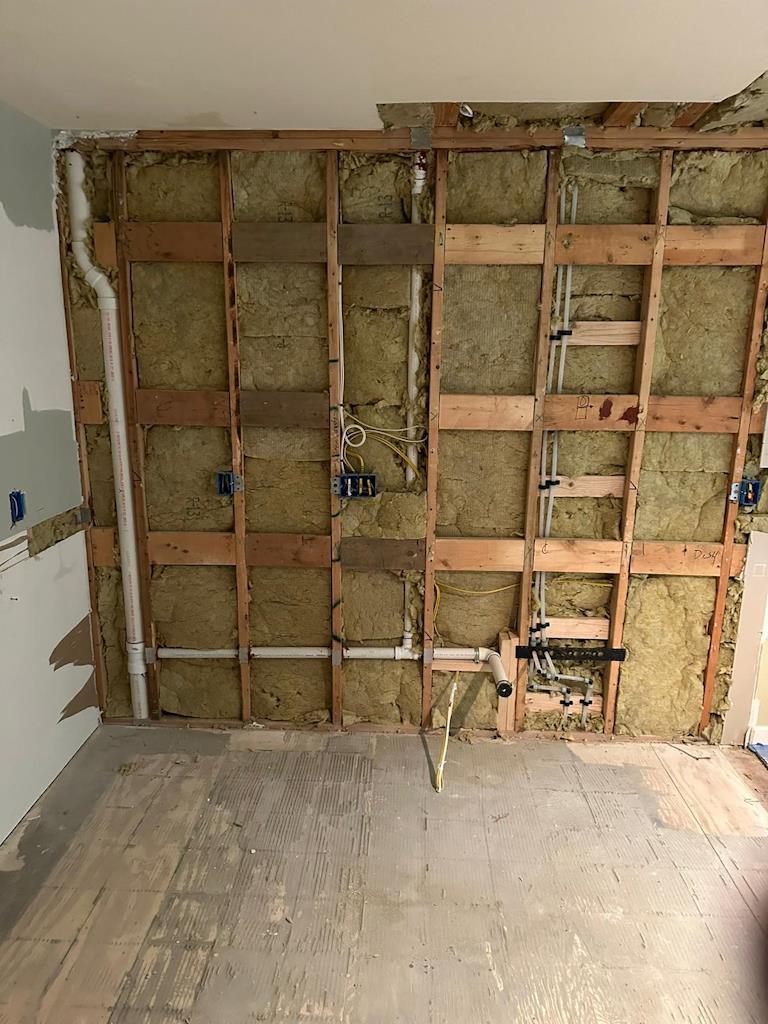 Kitchen remodeling in progress showing exposed wall framing and insulation with visible electrical and plumbing work.
