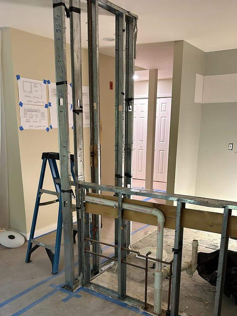During kitchen remodel featuring a partially framed wall with plumbing pipes and blueprints taped on the adjacent wall.
