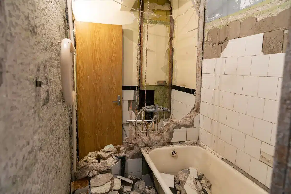 Gutted bathroom during a renovation in Boston showing demolition debris, exposed plumbing, and a bathtub ready for removal