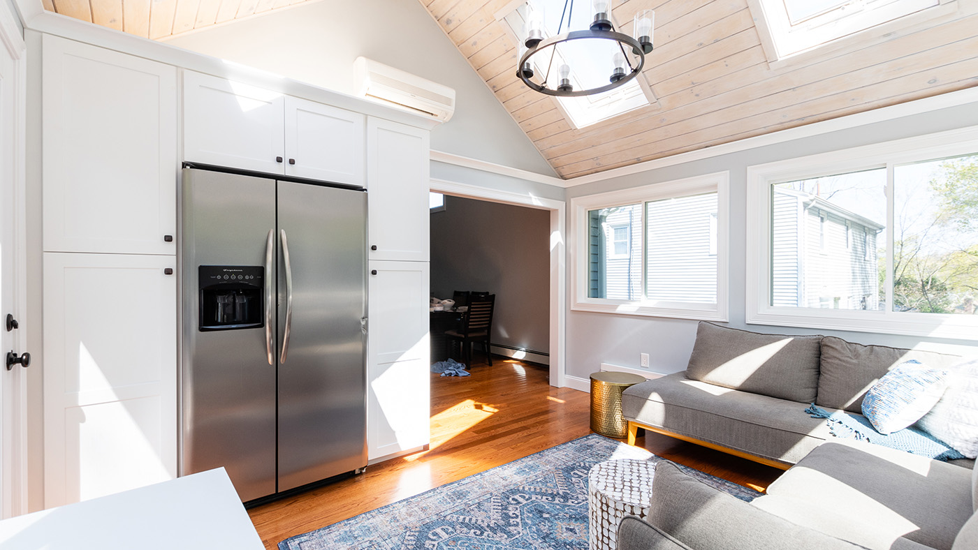 Floor-to-ceiling white shaker cabinets built in around the refrigerator in the Newtonville Ave. sunroom addition, under its vaulted plank ceiling and skylights.